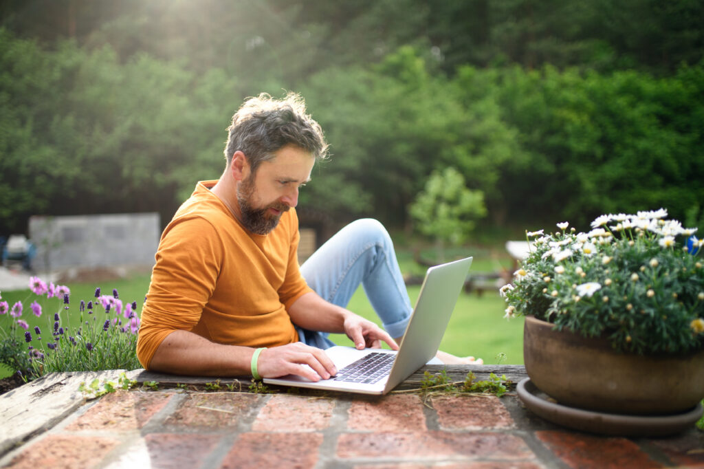 Mature man with laptop working outdoors in garden, home office concept in Best Advertising Ideas To Get More Landscaping Leads In 2024​ article